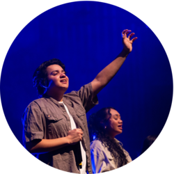 A student hold their hand out in worship while performing on stage at Vespers.